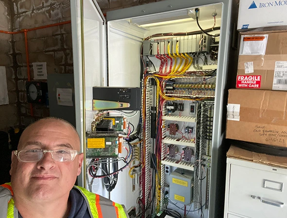 Our friendly specialist standing near a neatly organized indoor electrical panel and solar battery backup systems.