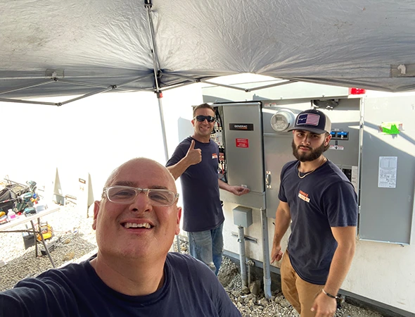 Two of our technicians standing outside near a large white unit while discussing solar battery backup systems.