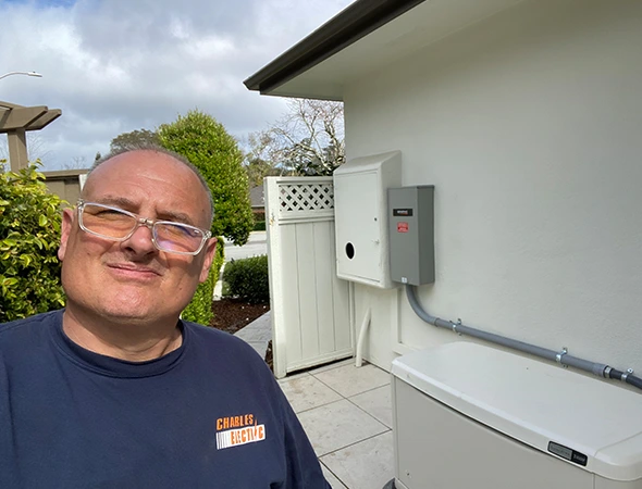 One of our team members smiling next to an outdoor wall-mounted unit for complete solar battery backup systems.